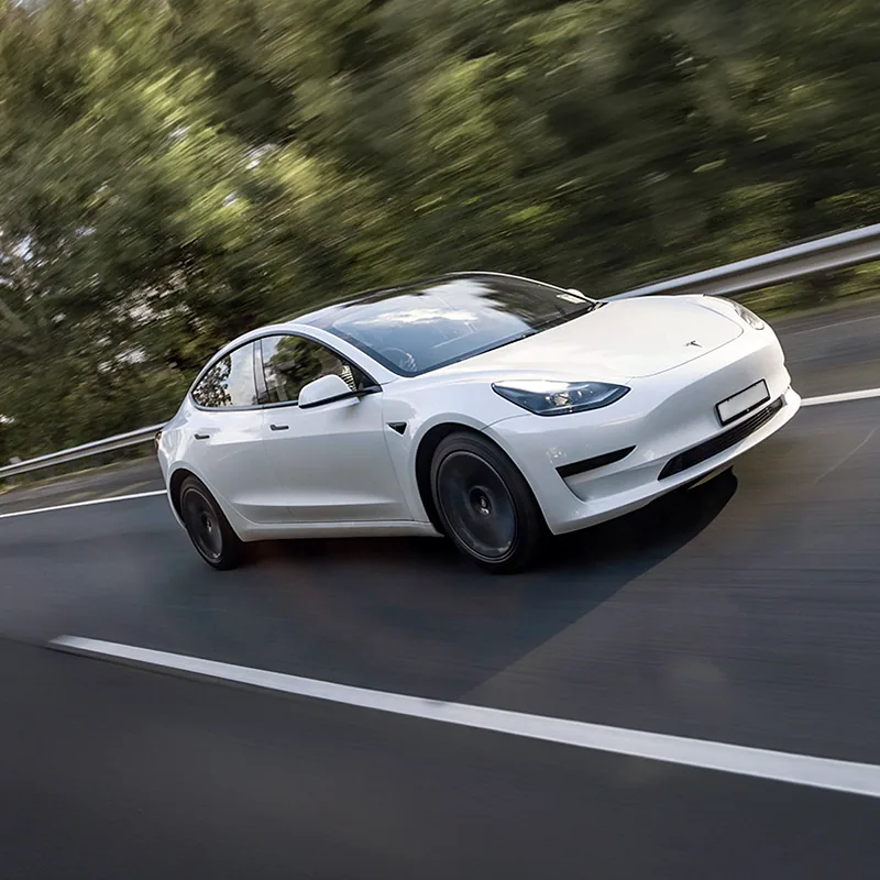 White Tesla sedan driving swiftly on a forest-lined highway with motion blur.