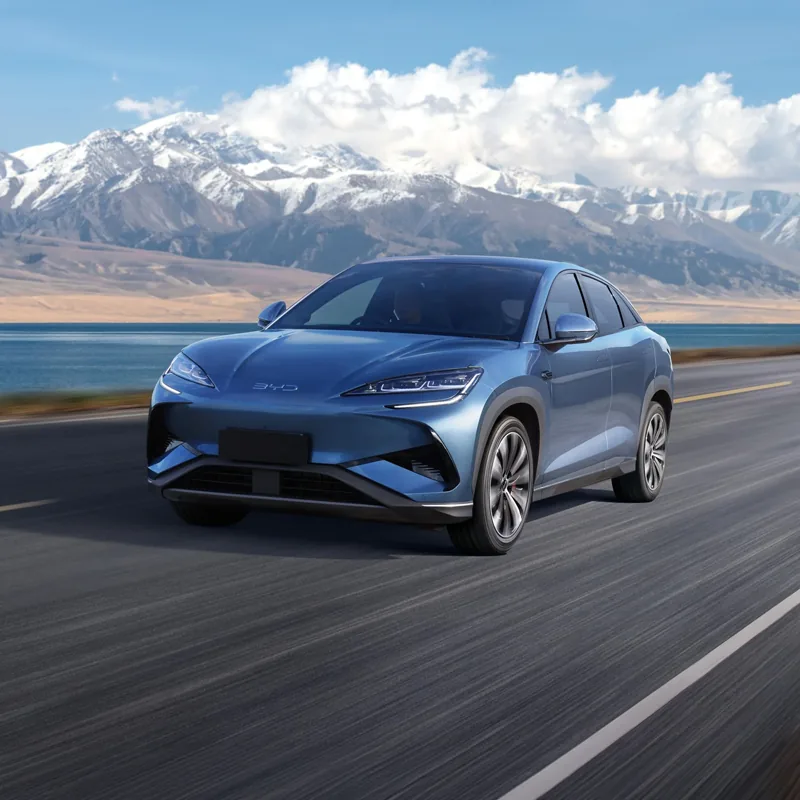 Blue BYD electric SUV driving on a road with snowy mountains and a lake in the background.
